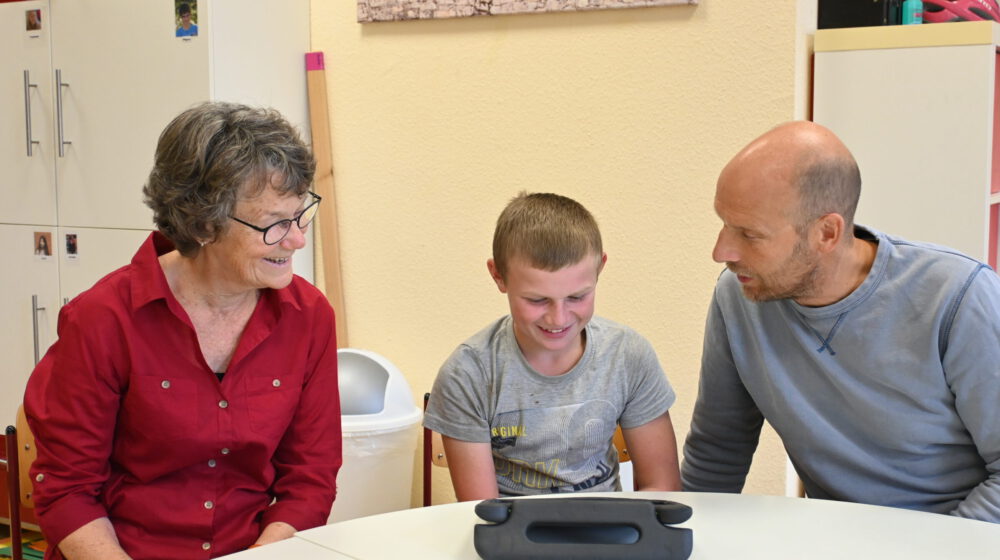 Unterstützungskraft und Lehrkraft begleiten einen Schüler bei der Arbeit mit Medien